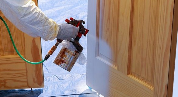 A professional painter wearing safety uniform and gloves applying polish on the doors by using a mechanized tool.